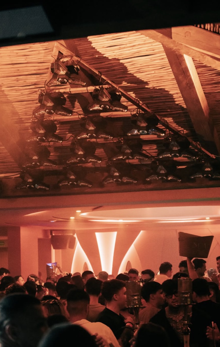 Sala de DŪA de noche, con el techo de cañizo iluminado y el público en una fiesta